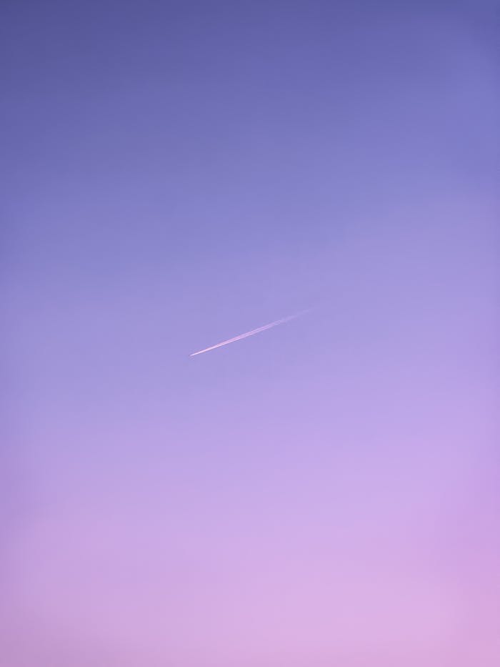 jet ascends through a pastel sky leaving a thin glowing contrail